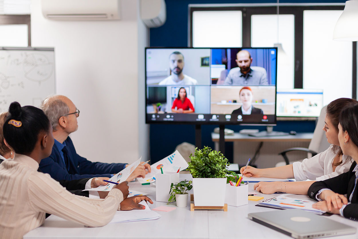 Multiracial employees meeting in conference room during video call.